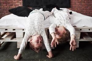 glückliche Kinder, die im schwarzen Schlafzimmer spielen. kleiner Junge und Mädchen, Bruder und Schwester spielen im Schlafanzug auf dem Bett foto