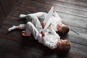 Kinder liegen im Schlafanzug auf dem Boden und zeichnen mit Bleistiften. süßes Kind malen mit Bleistiften