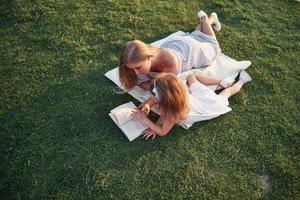 Mutter mit Kind liest ein Buch im Gras foto