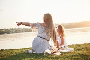 glückliche junge Mutter mit einer verspielten Tochter in einem Park am Wasser foto