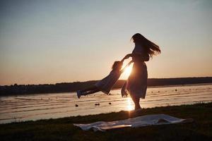 Mama spielt mit ihrem Baby im Urlaub am Meer, Silhouetten bei Sonnenuntergang foto