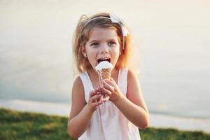 Ein hübsches kleines Mädchen isst ein Eis in der Nähe des Wassers foto