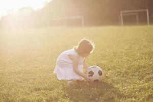 kleines Mädchen spielt bei Sonnenuntergang auf dem Feld Ball foto