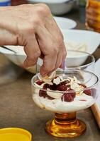 Koch vorbereiten Besondere Dessert mit frisch Creme, Kirsche, Kekse und Nüsse im ein Glas foto