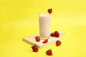 ein Glas von Milch mit Erdbeere Garnierung auf Schnitt Tafel isoliert Gelb Hintergrund foto