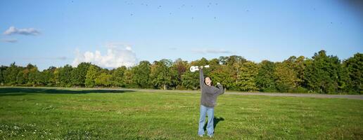 aufgeregt jung Frau Aufzug ihr Ukulele oben Über Kopf und lächelt, posieren mit Musical Instrument im Grün Feld Park foto