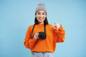 leidenschaftlich asiatisch Mädchen Fotograf, nehmen Bilder auf ihr Digital Kamera, Erfassen Momente draußen, Schießen Fotos, Blau Hintergrund foto