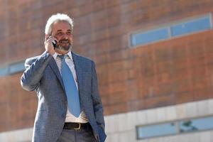 Senior Geschäftsmann mit Smartphone außerhalb des modernen Bürogebäudes. foto