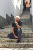 reifer Mann mit weißem Haar sitzt auf städtischen Stufen foto