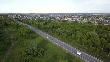 oben Aussicht von Autobahn Vorbeigehen durch Dorf mit Wald. Clip. Spur mit Vorbeigehen Autos auf Hintergrund von Dorf mit Grün Wald und Horizont mit Himmel foto