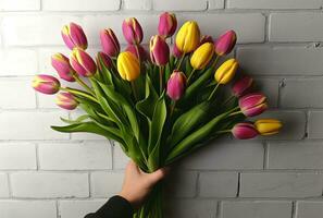 ai generiert männlich Hand halten ein Strauß von Tulpen im Vorderseite von Weiß Backstein Mauer foto