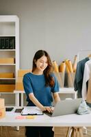 asiatisch Schneider Frau Arbeiten auf Kleider im Schneiderei Atelier. schön jung weiblich Mode Designer Lächeln im Studio foto