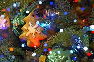 Weihnachten Baum dekoriert mit Lebkuchen Kekse, Grün Bälle, Licht Girlande. Lebkuchen Plätzchen im bilden von Weihnachten Baum mit Weiß Schneeflocke. Urlaub bunt verschwommen Bokeh Beleuchtung Hintergrund. foto