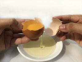 ein Frau Hand Risse ein Ei zu trennen das Ei Weiß und Eigelb und das Ei Schale im das Hintergrund. foto