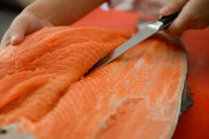 frisch Lachs Filet Nahansicht auf Weiß Schneiden Tafel Tabelle während Filetieren Lachs Bauch durch Koch im Kochen Zimmer foto