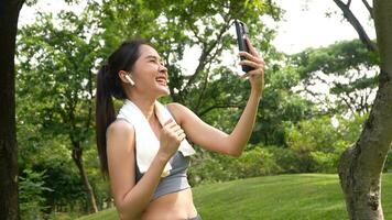 asiatisch Frau attraktiv verwenden Smartphone zum Video Konferenz mit ihr Freund nach trainieren. lächelnd sportlich jung Frau Arbeiten aus draußen und suchen beim Kamera. gesund Lebensstil Gut Sein Wellness foto