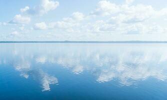 natürlich Landschaft, Wasserlandschaft mit groß Wasser Körper unter ein Blau Himmel mit Wolken und ein entfernt bewaldet Ufer foto