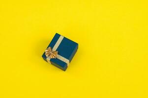 ein klein Geschenk Box mit ein Gold Band und ein Bogen auf ein Gelb Hintergrund. Geschenk foto