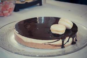 Schokoladen-Vanille-Mousse-Kuchen mit Schokoladenglas und zwei weißen Makronen foto