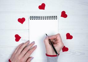 Frau Hand schreibt schreibt Herzliche Glückwünsche zu Valentinstag Tag. Liebe romantisch Botschaft. Flatlay Komposition. Valentinstag Tag Urlaub Konzept. oben Sicht. foto