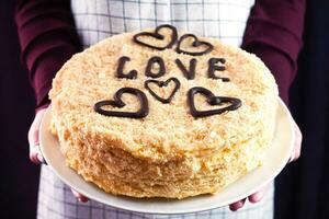 Frau hält Napoleon Kuchen mit Schokolade Herzen und Schokolade Inschrift Liebe. hausgemacht Kuchen zum das Urlaub. Nahansicht. foto