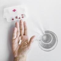 Die Hand der Person, die Tablette von der Pille-Organizer-Box mit weißem Hintergrund nimmt foto