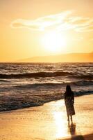 jung Dame Gehen im das Sonnenuntergang auf Santa Monica Strand foto