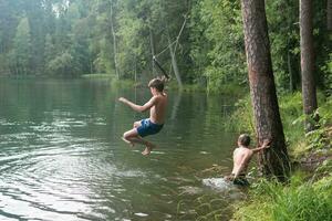 Jungs springt in das Wasser mit ein Tarzan schwingen während Schwimmen im ein Wald See foto