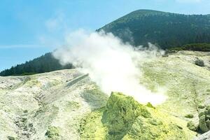 hell Rauchen Fumarole mit Schwefel Einlagen gegen das Hintergrund von das Mendeleev Vulkan Gipfel auf das Insel von Kunaschir foto