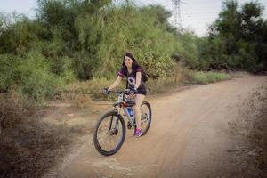 Frau, die auf dem Land Fahrrad fährt und in die Kamera schaut foto