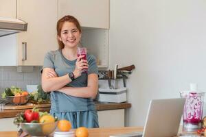 schön jung Frau im Übung Kleider haben Spaß im ein süß Küche beim heim. vorbereiten ein Vegetarier Obst Salat oder ein gesund Smoothie. foto