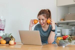 schön jung Frau im Übung Kleider haben Spaß im ein süß Küche beim heim. mit Ihre Laptop zu bereiten vegan Obst Salat Dressing, Obst zittert, oder gesund Smoothies. foto