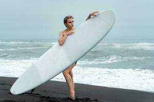 weiblich Sport Mode Modell- halten Surfbrett und Stehen hinter Es, Konzept von aktiv Lebensstil foto