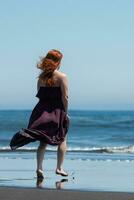 atemberaubend Aussicht von das Frau im das lange Kleid Gehen gegenüber das Kristall Blau Meer auf das sandig Strand foto