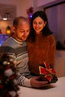 Mann überraschend Freundin mit Weihnachten Geschenk Geschenk mit Band auf es feiern Weihnachten Urlaub im Weihnachten dekoriert Küche. glücklich froh Familie genießen Winter Jahreszeit zusammen foto