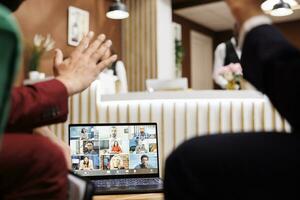 zwei Angestellte mit Videoanruf Fernbedienung während Sie warten zum Zimmer zu Sein bereit, Teilnahme Geschäft Treffen Telefonkonferenz. Unternehmer reden zu Kollegen im Hotel Empfangshalle, Telearbeit. foto