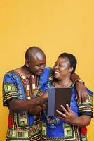 glücklich afrikanisch amerikanisch Paar im Liebe Umarmen während mit Digital Tablette zusammen. heiter reifen Freund und Freundin tippen auf Gerät Berührungssensitiver Bildschirm und Scrollen Internet Seite foto
