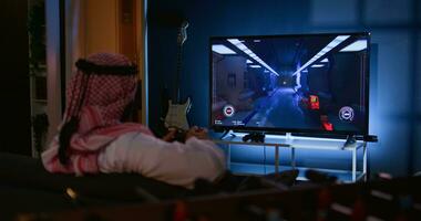 Arabisch Mann spielen Einzelspieler Videospiele auf Fernseher, entspannend nach lange Tag beim arbeiten. Mitte östlichen Spieler genießen Wissenschaft Fiktion Schütze Spiel auf Spielen Konsole, haben Spaß foto