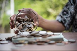 Hand, die Münzen in ein Glas mit Geldstapel setzt, wächst das Wachstum und spart Geld
