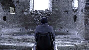 Rückseite Aussicht von ein Mann im ein Rollstuhl zum das deaktiviert im das ruiniert Kirche. Filmaufnahme. das Konzept von Verlust foto