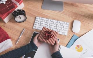 Geschäftsfrau Hand hält Geschenkbox in Weihnachtsferien im Büro mit Weihnachtsdekoration auf dem Tisch. foto