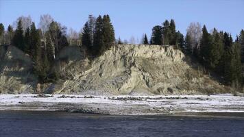 natürlich Landschaft mit ein Fluss im früh Winter und ein hügelig Ufer bedeckt durch Bäume. Clip. Stein Cliff mit Wald und kalt Fluss. foto