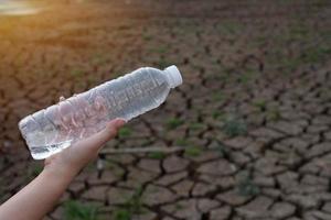 Nahaufnahme der Frauenhand, die die durchsichtige Plastikflasche am Rissbodenhintergrund hält