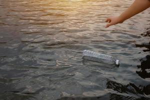 Frauenhand, um die gebrauchte Plastikmüllflasche auf dem Wasser in einem Kanal aufzuheben foto