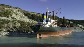 Antenne zum ein leeren industriell Schiff festgemacht in der Nähe von Meer Ufer mit viele Menschen Gehen auf ein Strand. maritim Ladung Schiff Stehen in der Nähe von Grün Bäume Steigung im ein Sommer- sonnig Tag. foto