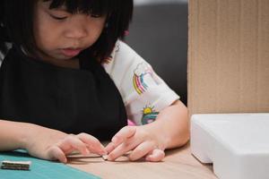 Porträtkind lernen, Kleben zusammenzukleben. Vorschulkind, das Klebestift auf Karton für Schulhausaufgaben setzt. kleines Mädchen, das ihre Hände benutzt, um ein süßes Zuhause für ein DIY-Projekt zu machen. selektiver Fokus.