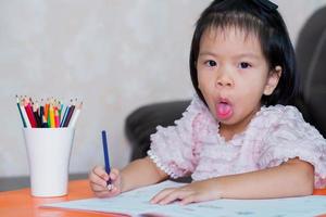 Kind machte ein lustiges Gesicht und streckte eine lustige Zunge heraus, als sie in ihrem Hausaufgabenheft malte. Kinder im Alter von 4-5 Jahren. foto
