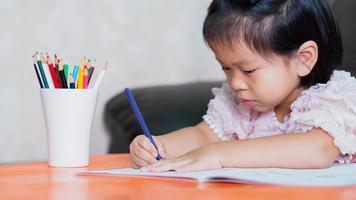 kleines Mädchen, das zu Hause Kreativitätsentwicklung zeichnet, Handdetail einer kleinen Kinderzeichnung mit bunten Bleistiften.