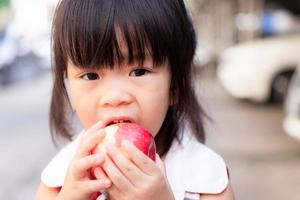 Porträt des Kindermädchens, das roten Apfel isst und Kamera betrachtet. Kopf ohne gesundes Kind, das frisches Obst für die Snackzeit isst. Kinder im Alter von 3 Jahren. foto