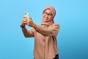 Porträt einer aufgeregten, fröhlichen jungen Asiatin, die Handy benutzt, macht Selfie auf blauem Hintergrund foto